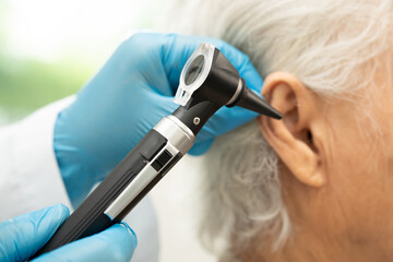 Audiologist or ENT doctor use otoscope checking ear of asian senior woman patient treating hearing...