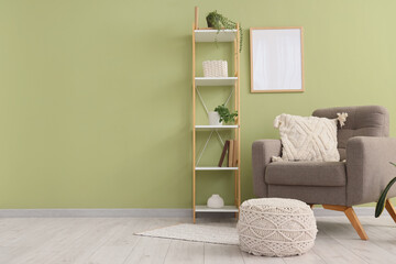 Armchair, shelving unit and pouf near green wall in room