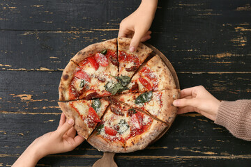 Female hands taking slices of delicious pizza Margarita on black wooden background. Top view