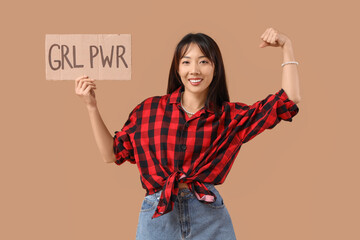 Young happy Asian woman holding paper with text GIRL POWER and showing muscles on beige background....