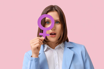 Surprised young woman holding female symbol on pink background. Women's history month