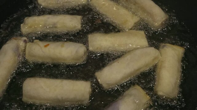 High angle closeup of springrolls frying in hot oil in stovetop pan