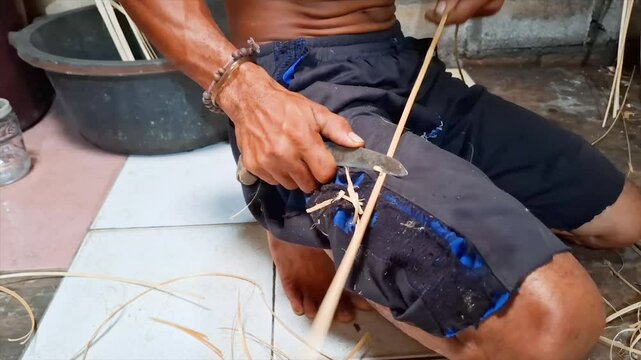 Close-up shot of a skilled craftsman's hands carefully splitting bamboo strips using a sharp knife.