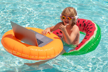 Happy little boy learning online computer laptop. Child relax and rest on colorful inflatable ring using computer in swimming pool. Summer business and technology. Summer office and freelance concept.