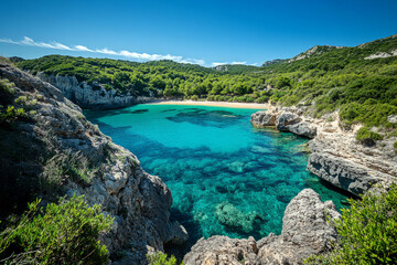 Obraz premium Secluded turquoise bay with crystal clear water surrounded by rocky cliffs and lush greenery under blue sky