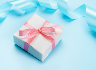 White gift box with pink bow on blue background with ribbon. Valentine or Mother's Day.