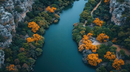 Obraz premium Aerial view of a serene river winding through vibrant autumn foliage and rocky cliffs
