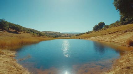 Naklejka premium Serene rural pond reflecting sun, dry hills background, idyllic landscape