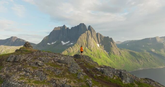 Drone crane over hiker reveal majestic jagged Senja mountain by fjord in sunset