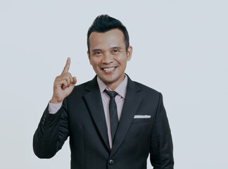Asian boss manager businessman smiling at the camera with one hand pointing up, isolated over white background.