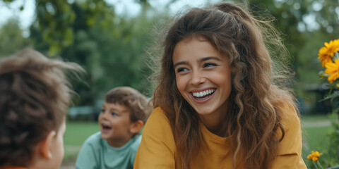Fototapeta premium Woman with curly hair in yellow sweater playing with children in garden. Family lifestyle content