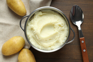 Mashed potatoes in pan, spoon and potatoes on towel on wooden background, top view