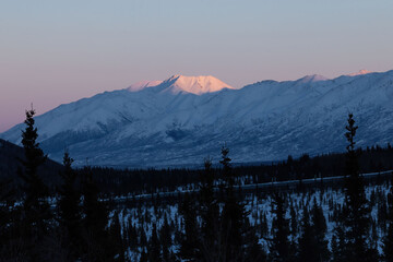 Sun shininig on top of snowy mountaintop behind pipeline in Alaska
