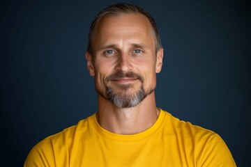 Obraz premium Confident man with a beard smiles in a bright yellow shirt against a dark backdrop