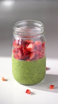 Overnight Oats Matcha being topped with strawberry on white table with morning shadow