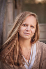 Portrait of a girl with light, fair hair of Slavic appearance. Beautiful girl with long hair. Girl in a brown jumper sits on a wooden staircase and looks at the camera, smiling slightly