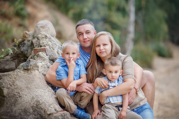 Summer evening. Happy and beautiful family on a walk. Dad, mom and two sons hugging each other are sitting near a large stone. Two brothers. Older and younger brother. Family portrait