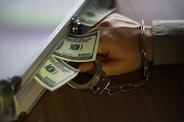 Handcuffed Hand Grasping Cash from Aluminum Briefcase on Wooden Table