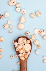 Top View of Makhana or Fox Nut in a Wooden Spoon Isolated on Light Blue Background with Copy Space in Vertical Orientation, Also Known as Lotus Seed Pop, Euryale Ferox or Gorgon Nut