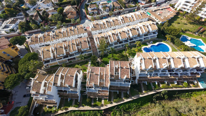 Fototapeta premium Aerial drone photo of the beautiful town of Sitio de Calahonda in Malaga Spain showing a bird's eye view of residential and holiday homes with swimming pools from above on a sunny day