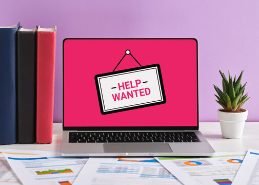 Laptop showing help wanted sign on pink screen with documents on desk