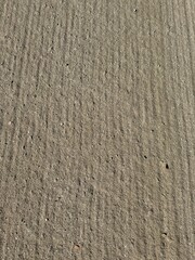 Close-up of a sandy surface with natural ripples and scattered small pebbles. The texture is shaped by wind or water, creating an organic pattern ideal for backgrounds or nature-themed designs.