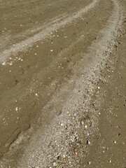 A road on the beach, where path is shown by white pieces of shells and pebbles, with other sand being more brown in colora