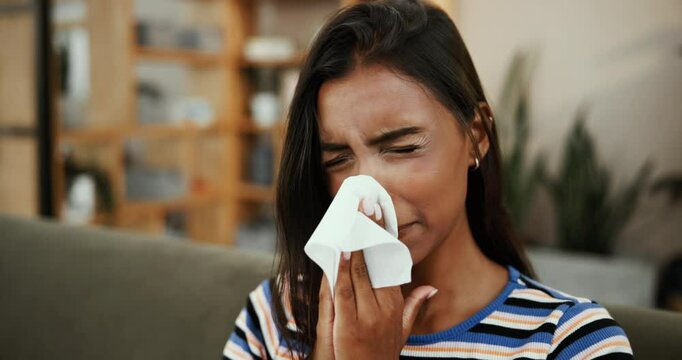Sneezing, sick and woman in living room, home and tissue for hay fever on couch and blowing nose. Lounge, infection and person with allergies in house, flu and health trouble with sinusitis illness