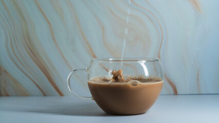 Pouring cream into a cup of coffee against a marbled background in a tranquil setting