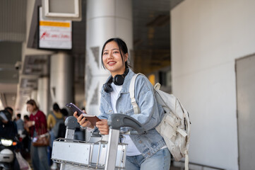 A beautiful Asian female traveler stands at the airport taxi pickup point, looking for her taxi. © bongkarn