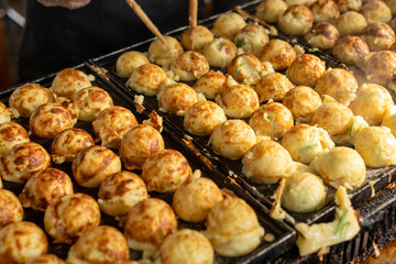 Fresh hot Takoyaki, a Japanese street food, being prepared with careful skill on a hot plate using wooden sticks. A delightful scene showcasing the intricate culinary process of creating these savory