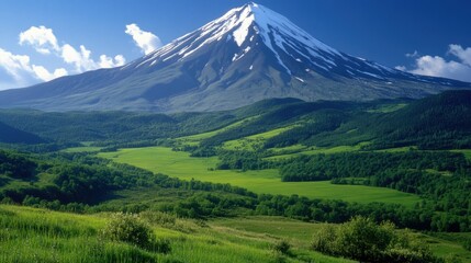 This image captures a serene mountain valley with Mount Fuji in the background, bathed in sunlight on a clear day. The scene is dominated by the verdant slopes of the valley, where lush green fields