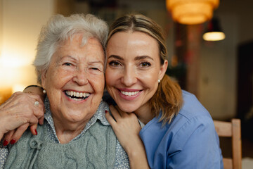 Portrait of caring healthcare worker visiting a senior patient at home, hugging her.