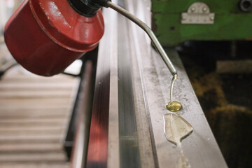 Applying lubricating oil to a metal surface using a red oil can in an industrial workshop, ensuring...