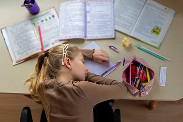 Exhausted girl sleeping on homework at the desk, Young girl falls asleep over her homework,...