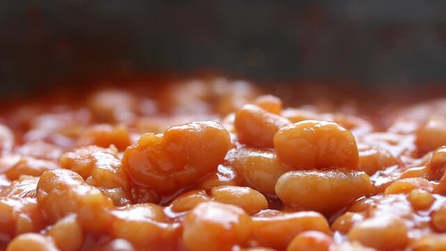 Cooking baked beans in boiling tomato sauce on black background. Close-up view
