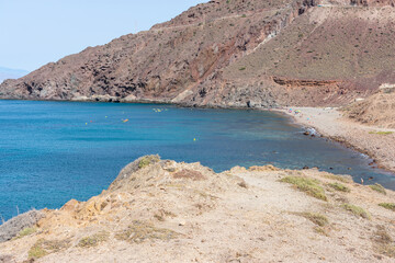 beach between hills with bathers in the sand and canoes in the sea