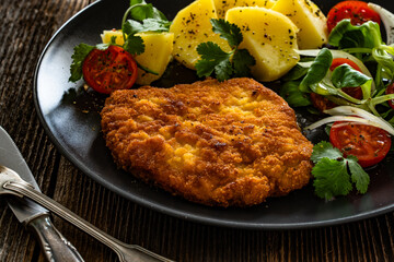 Breaded fried pork chop with fresh vegetable salad and potatoes on wooden table	