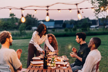 Friends enjoying outdoor dinner party with string lights at sunset