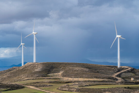 Wind turbines dotting a scenic hillside with winding paths under expansive skies in La Muela, Zaragoza, Spain, exemplifying renewable energy in natural landscapes.