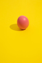Minimalist vertical image of a pink painted Easter egg on a yellow background, Easter decoration concept