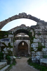 Naklejka premium Ancient stone arches of a moss-covered ruined church, leading to an interior with a crucifix, radiating a historic and sacred atmosphere 