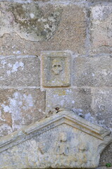 Weathered stone wall with ancient carved figures and skull symbol, conveying a sense of history and mystery in an outdoor setting
