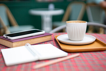 Coffee cup with book for read and mobile phone,  diary book on table at outdoor cafe in the morning