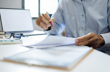 asian businessman reviewing document at office workplace with computer laptop. legal expert, professional lawyer reading and checking financial documents or insurance contract