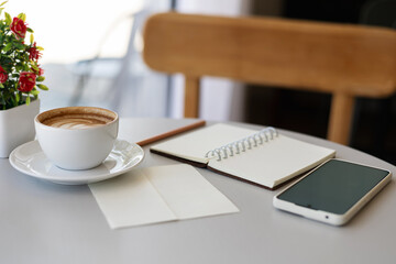 Close-up shot, latte coffee with mobile phone and note book on white table, relax in the morning in cafe before work