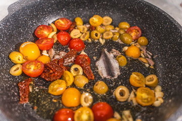 Cook the spaghetti Puttanesca, fry the tomatoes, anchovies, olives and capers with garlic in a pan. Close-up.
