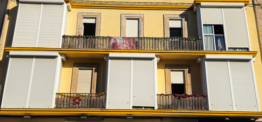 Jerez de la Frontera; yellow residential building with white shutters, balconies, some open...