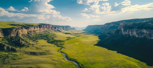 Aerial view of a stunning montana valley with green grass, river, and rocky cliffs on sunny day.