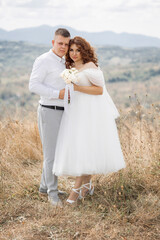 A bride and groom are standing on a grassy hillside